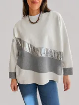 Buzo de tejido de punto con diseño oversize y calce relajado. Presenta un diseño de bloques de color en tonos neutros con una franja diagonal central en material metalizado brillante. Cuenta con cuello redondo y mangas largas con puños acanalados.