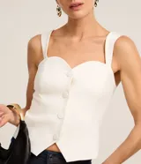 Blusa de sastrería color blanco, sin mangas, con escote corazón, breteles anchos y cierre frontal con botones forrados. Presenta un dobladillo en punta y espalda elástica.