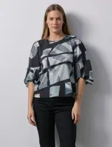 Blusa de gasa con estampado geométrico en tonos negro, gris y celeste. Tiene cuello redondo y mangas 3/4 amplias con abertura y botón.