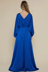 Vestido largo de fiesta confeccionado en satén azul brillante, con cuello redondo, mangas largas abullonadas con puños ajustados y falda con tajo lateral profundo.