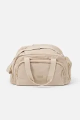 Bolso de viaje tipo duffel color beige, con compartimento principal con cierre, bolsillo frontal con cierre y doble asa de mano. Incluye correa ajustable para el hombro y detalle de logo grabado en el frente.