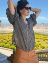 Camisa de gasa color gris oscuro, con mangas globo y una tira central vertical decorada con piedras azules.