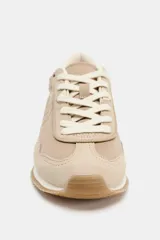 Zapatilla deportiva tipo running en tonos beige y crema, con combinación de materiales como gamuza y tela. Presenta pespuntes decorativos en el cuerpo, cierre de cordones y punta redonda. La suela tiene una altura de 3 cm.