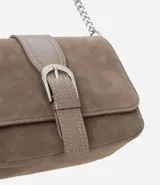Cartera bandolera pequeña de estructura rígida en gamuza sintética color marrón. Presenta una tapa frontal con detalle de tira central y hebilla decorativa, y una correa larga de cadena metálica.