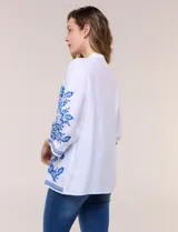 Blusa blanca con bordados florales en azul, de manga tres cuartos y cuello mao con escote en V.