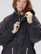 Campera tipo piloto con capucha, cierre frontal con botones y detalle de costuras en zigzag. Presenta cordones ajustables en la cintura y capucha, puños elásticos y logo bordado en el pecho.