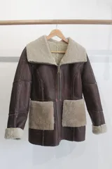Campera reversible de cuero genuino napalán en color marrón, con detalles de corderito sintético beige en el cuello, los bolsillos frontales, los puños y el interior. Cuenta con cierre frontal y bolsillos aplicados.