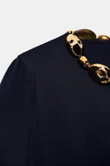 Top de punto azul marino de manga corta abullonada, con cuello redondo decorado con aplicación de bolas doradas y cierre en la espalda con abertura y botón oculto.