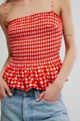 Musculosa de cuadros vichy rojos y blancos, con cuerpo fruncido elastizado, escote recto, tirantes finos y diseño peplum con vuelo en el ruedo.