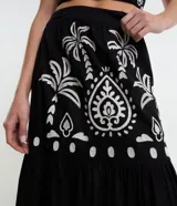 Pollera midi de algodón con diseño acampanado y cierre lateral. Presenta un estampado contrastante de palmeras y motivos arabescos sobre fondo oscuro.