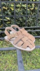 Sandalias de cuero marrón con diseño de tiras entretejidas y hebilla lateral.