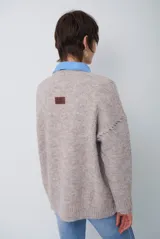 Buzo de punto color beige con diseño de trenzas y costuras decorativas en contraste que forman rombos. Presenta cuello redondo, mangas largas y puños acanalados.