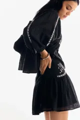 Pollera corta negra de tejido liviano con efecto arrugado y detalles bordados florales en blanco en los paneles laterales superiores. Presenta cintura clásica con cierre oculto y costura fruncida que genera vuelo en la parte inferior.