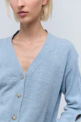 Cárdigan corto celeste de lana con lentejuelas, escote en V, cierre frontal con botones y mangas largas con aberturas.