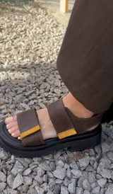 Sandalias marrones con tiras de cuero con ajuste de velcro y detalles en amarillo.