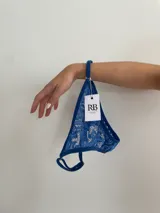 Conjunto de lencería compuesto por un top bralette de encaje azul con breteles ajustables y bombacha tipo less de encaje regulable en los laterales.