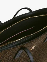 Cartera tipo tote de Tommy Hilfiger con diseño jacquard de monogramas TH en color marrón y laterales en negro. Cuenta con asas superiores fijas y logo metálico dorado en el frente.