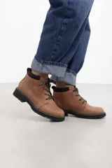 Borcego de cuero vacuno color marrón caramelo con acabado mate, estilo combate y caña baja. Cuenta con cordones marrones, panel de gamuza oscura en el cuello y suela de caucho negra tipo tractor con costura blanca visible.