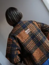 Saco abrigado de tejido texturizado en tonos marrones y negros, con diseño a cuadros, ribetes de lino en los bordes y cierre frontal con lazos.