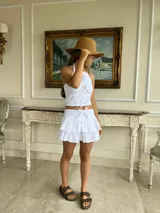 Top blanco confeccionado en algodón con cuello halter y detalle de tres lazos decorativos en el frente. Posee una textura ligera y un diseño romántico ideal para el verano.