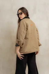Campera color beige con cuello de corderito negro, cierre frontal con botones y forro interior. Presenta un diseño de corte recto y mangas largas con puños vueltos.