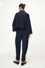 Pantalón de tiro alto confeccionado en denim oscuro, con pinzas delanteras que aportan volumen y pernera abullonada. Cuenta con bolsillos frontales, falsos bolsillos traseros con solapa y bajo ajustable mediante botones a presión.