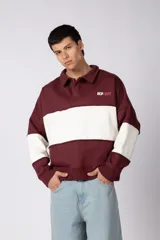 Buzo tipo polo de calce relajado con diseño de bloques de color en bordó y blanco. Presenta cuello camisero, cierre frontal parcial con botones ocultos y logo bordado en el pecho.