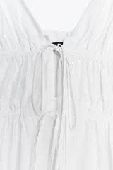 Vestido midi blanco de popelín con escote pico pronunciado, tirantes finos ajustables con cordones y detalle de frunces en la cintura.