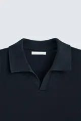 Jersey de punto color verde oliva, de calce relajado (relaxed fit), con cuello solapa y abertura frontal en forma de V. Es de manga corta y presenta acabados en rib en puños y ruedo.