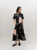 Vestido midi de popelina de algodón negra, con estampado floral en tonos rosados y blancos, cuello tipo bebe, mangas cortas, cierre frontal abotonado y bolsillos laterales.
