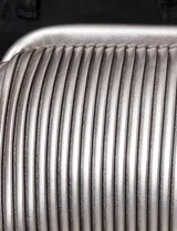 Cartera tipo clutch de mano con diseño estructurado y silueta redondeada. Presenta un acabado plateado metalizado con textura de plisado tubular vertical y cierre de marco rígido.