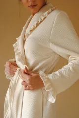 Bata larga color blanco, confeccionada en algodón capitoneado con diseño de espiga. Presenta volados en el cuello y puños, y lazo de ajuste en la cintura.