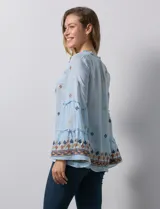 Blusa celeste de gasa bordada, con escote en V y lazo de ajuste. Mangas largas con terminación amplia.