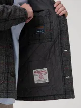 Chaqueta de lana Harris Tweed color gris con patrón de tartán, cuello camisero, cierre frontal de botones y bolsillos aplicados.
