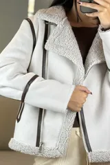 Campera tipo gamulán de color crema con interior y cuello de corderito sintético. Presenta cierre frontal cruzado, bolsillos laterales con cierre y detalles de costuras en contraste color marrón oscuro.