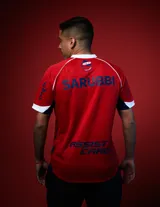 Camiseta de fútbol Umbro del Club Nacional de Football, modelo Away 2026. Diseño en color rojo con detalles en azul y blanco en el cuello y mangas. Incluye logo de Umbro, escudo del club y sponsors estampados en el frente y mangas.