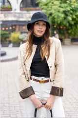 Chaqueta corta color beige, con cuello redondo, cierre frontal con botones dorados, bolsillos de parche y puños en contraste color marrón.