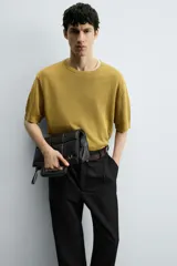 Bolso tipo shopper de diseño acolchado con patrón de cuadros, confeccionado en material sintético negro. Presenta asas de mano integradas en la estructura superior y un detalle de borla colgante con herraje metálico.