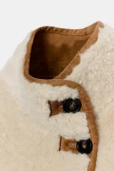 Cazadora reversible de cuello subido y manga larga, confeccionada en tejido efecto borreguillo con detalles en contraste efecto ante. Cuenta con cierre frontal de botones y bolsillos delanteros.