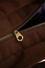 Bolso tipo tote bag color marrón con diseño capitonado de ondas, asas largas y placa metálica con el logo de la marca.