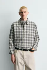 Camisa de corte boxy fit confeccionada en tejido de algodón con elasticidad. Presenta un diseño a cuadros, cuello solapa, manga larga con puños abotonados, bolsillo de vivo en el pecho y cierre frontal con botones.