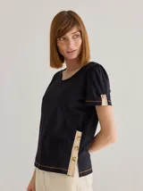 Remera color crema de algodón y lino, con cuello en V y mangas cortas abullonadas. Presenta cartera decorativa de botones en cuerpo y mangas.