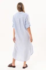 Vestido camisero largo color celeste, de silueta relajada con abotonadura frontal completa, cuello camisero y mangas regulables. Presenta tajos laterales y detalle de bordado sutil en la manga.