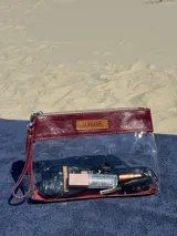 Necessaire transparente con detalles en cuero bordó, cierre superior con cremallera y correa de mano.