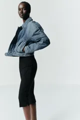 Cazadora de denim estilo crop con cuello solapa, manga larga y cierre frontal con cremallera y botón metálico. Presenta bolsillos de vivo en el delantero y detalle de trabillas en los hombros.