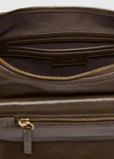 Bolso de hombro estilo hobo en color marrón oscuro con acabado brillante. Presenta un diseño estructurado con múltiples bolsillos exteriores con cierre frontal y laterales, herrajes metálicos dorados y asa fija.