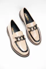 Mocasín de cuero vacuno en color arena con detalles en negro, presenta un adorno metálico en el empeine y suela plana de goma.