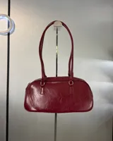 Cartera tipo baguette de cuero sintético color borgoña, con doble asa corta y cierre superior con cremallera.