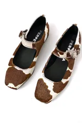 Zapato Mary Janes de cuero con estampado de vaca en tonos marrón y blanco, con correa sobre el empeine y hebilla metálica.