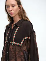 Camisa larga de diseño patchwork con cierre frontal de botones, confeccionada en una combinación de texturas lisas y estampados florales con detalles bordados en el canesú y los puños.